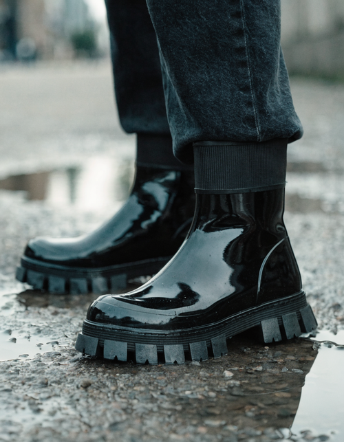 Black rubber ankle boots with ribbed collar and lug outsole on wet ground after rain