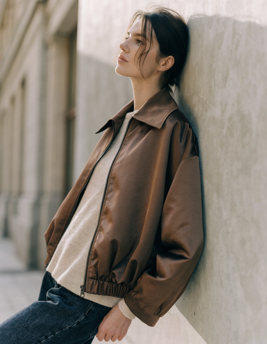 Woman wearing a brown zip-front bomber jacket with spread collar over a cream knit