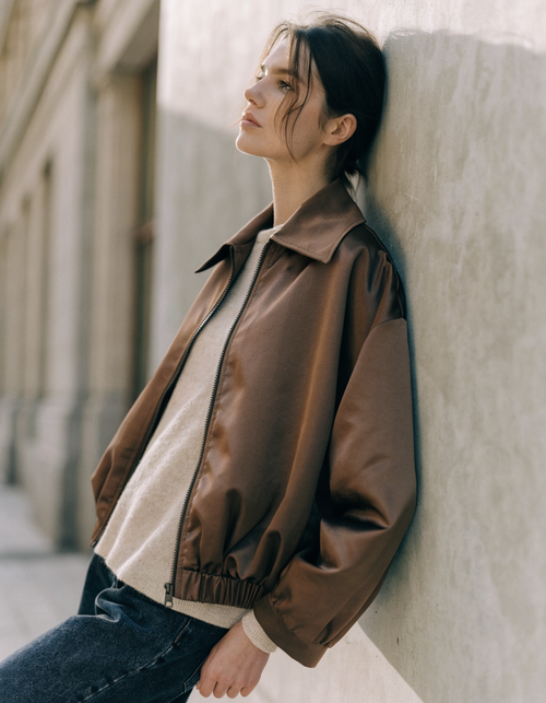 Woman wearing a brown zip-front bomber jacket with spread collar over a cream knit