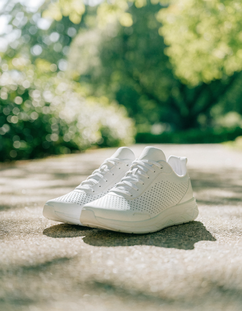 White perforated lace-up athletic sneakers on a sunlit park path