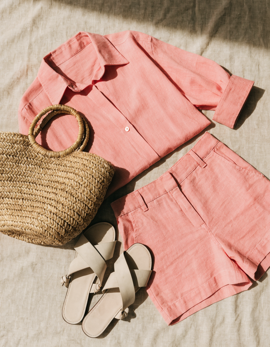 Flat-lay of the pink woven shirt and matching shorts with a straw bag and sandals