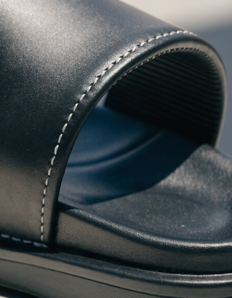 Detail of the contrast edge stitching and contoured footbed of a black slide sandal