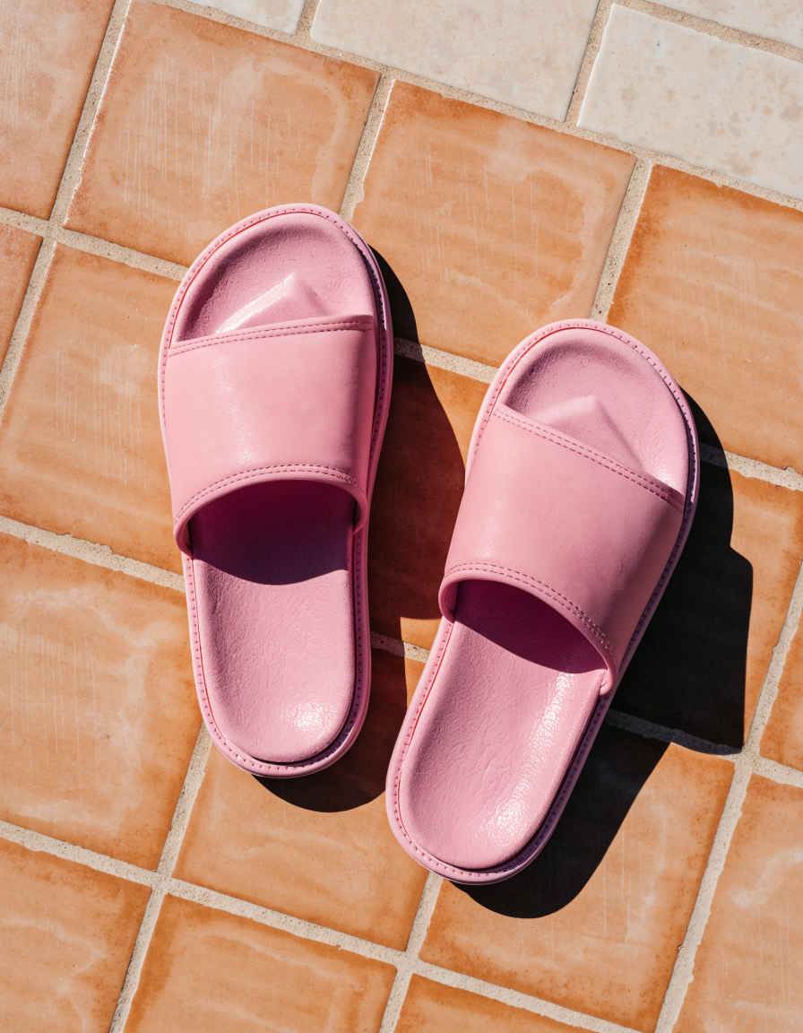 Pink slide sandals with a wide cushioned band, top-down on poolside tiles