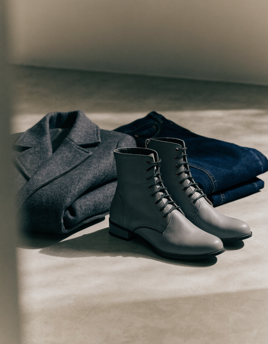 Grey lace-up ankle boots styled beside a folded wool coat and jeans