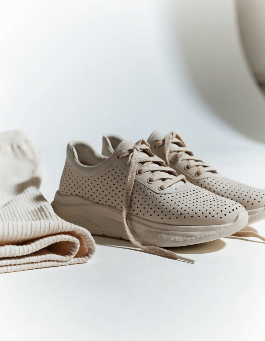 Beige perforated lace-up sneakers angled beside folded cropped joggers