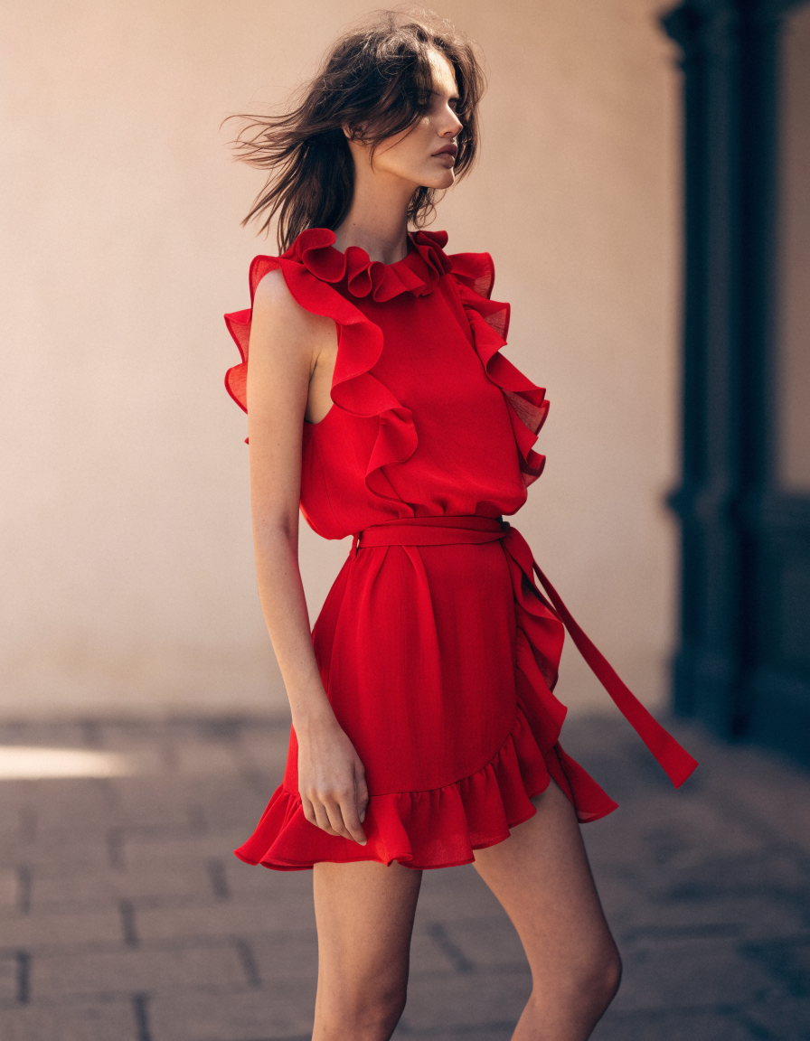 Three-quarter view of the red tie-waist ruffle mini dress in soft daylight