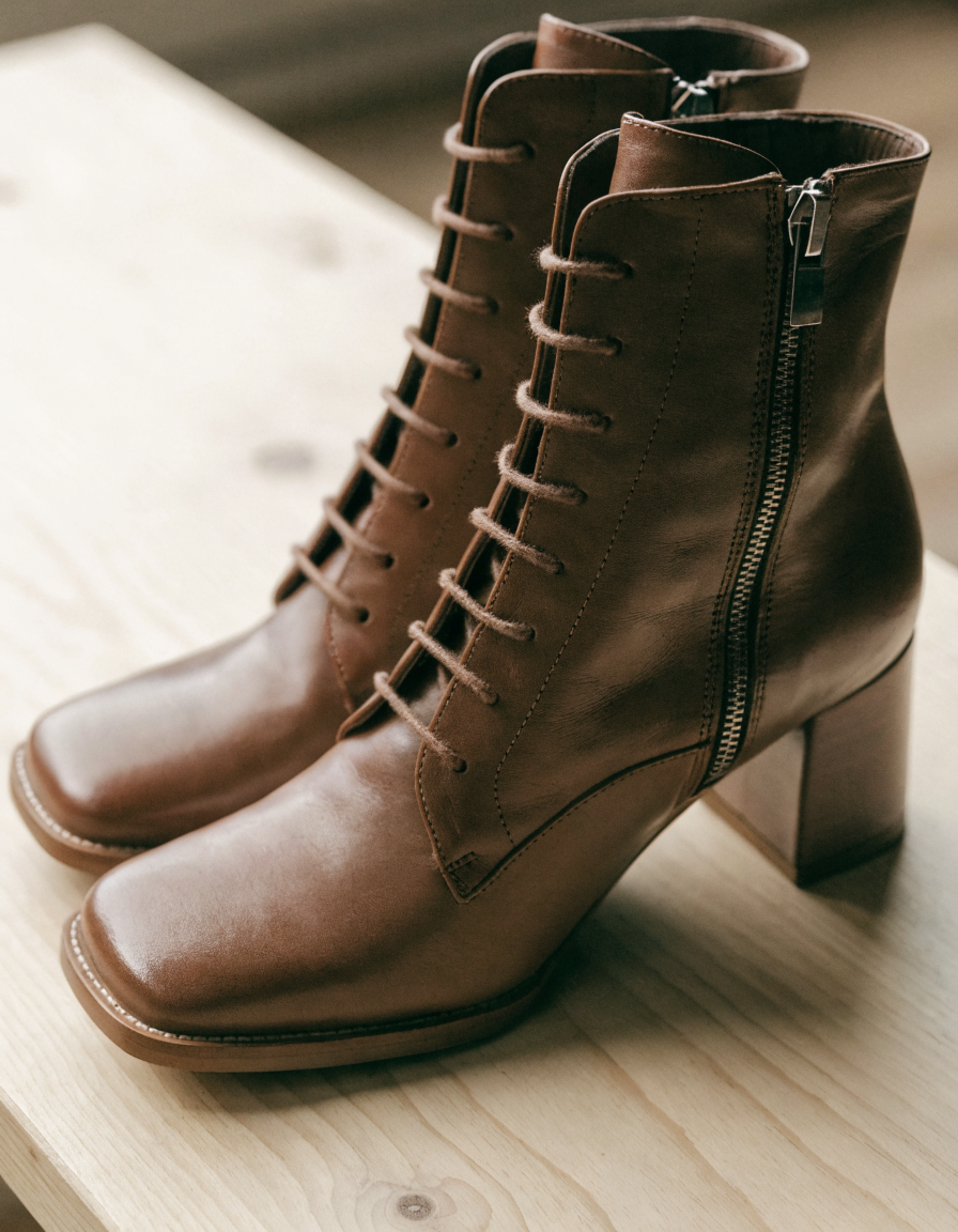Brown lace-up ankle boots with side zip, three-quarter angle on pale wood