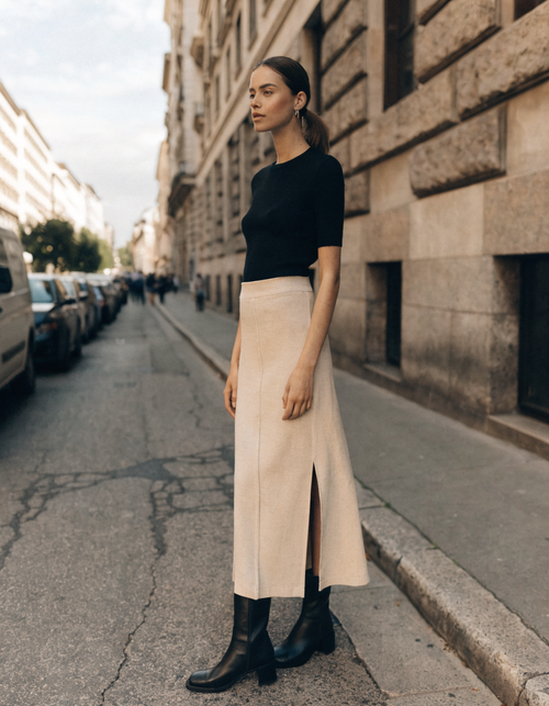 Woman wearing a cream panel seam midi skirt with a fitted black knit top