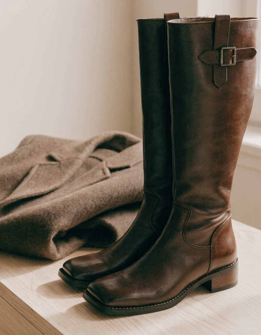 Dark brown knee-high boots angled beside a folded wool coat