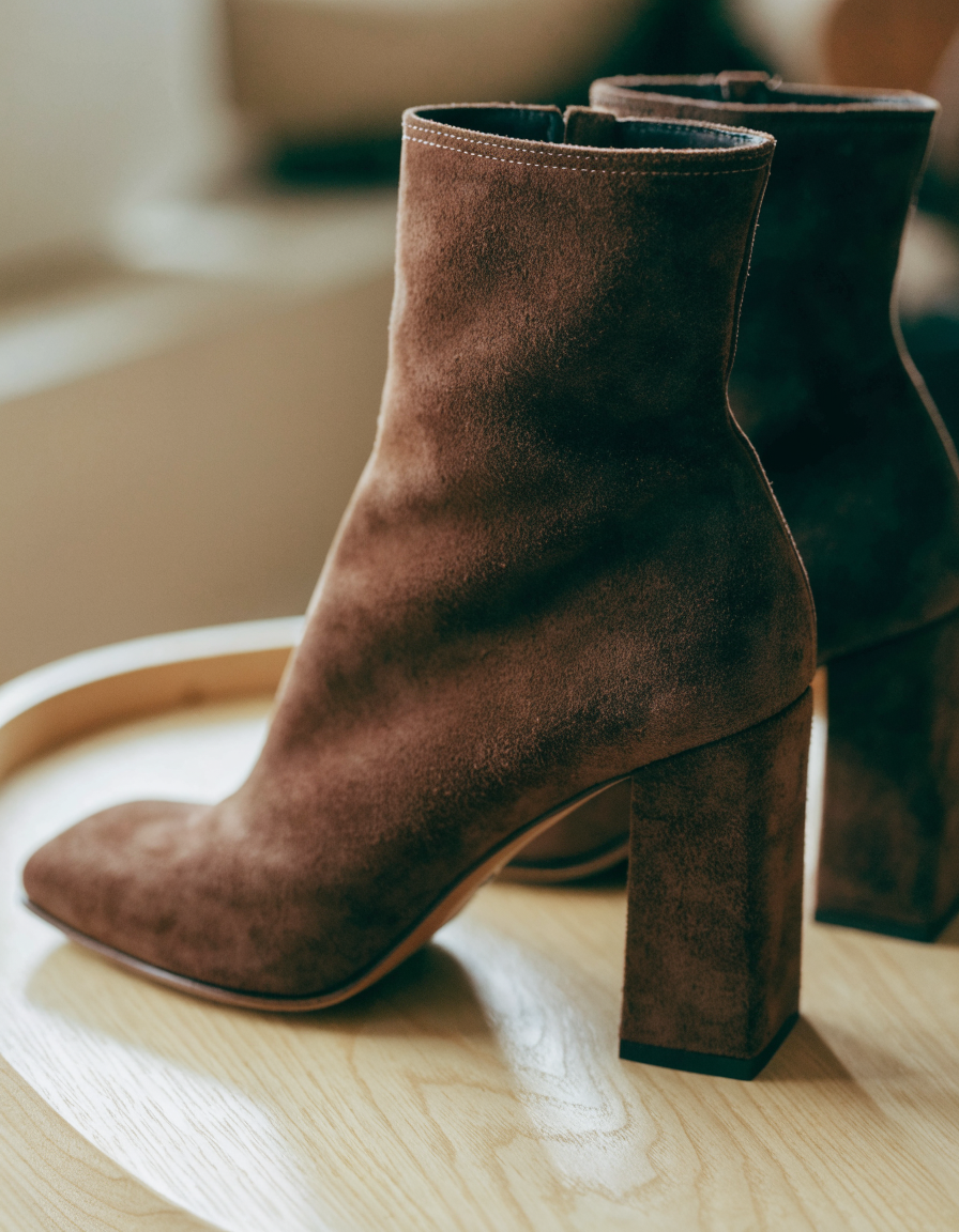 Dark brown square toe ankle boots at a three-quarter angle on pale wood