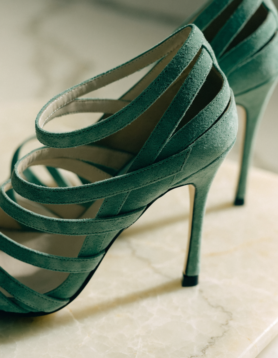 Green suede-look multi-strap dress heels in side profile on pale marble