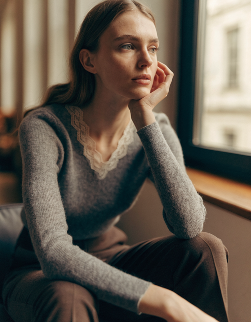 Woman wearing a gray fine-knit sweater with a lace-trimmed V-neckline and tailored trousers